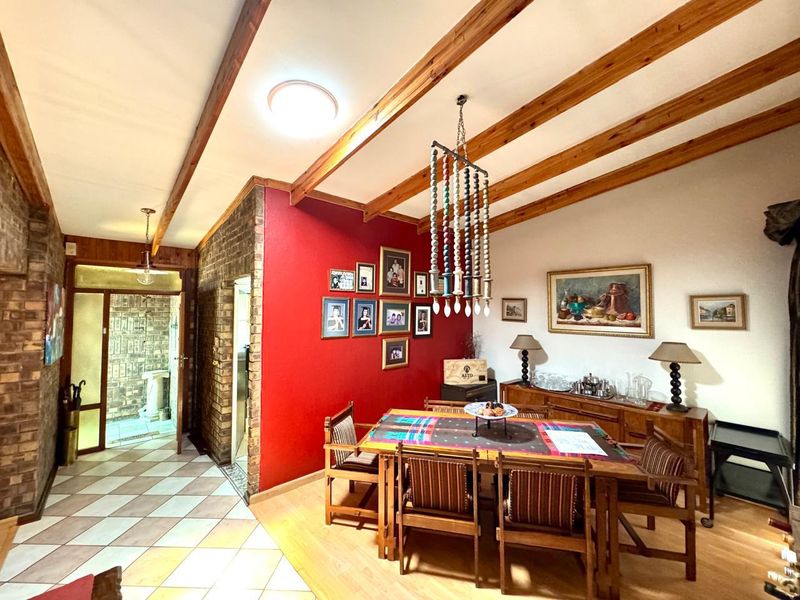 Dining room featuring exposed timber ceiling beams, a brick feature wall, and a combination of tiled and laminate flooring.