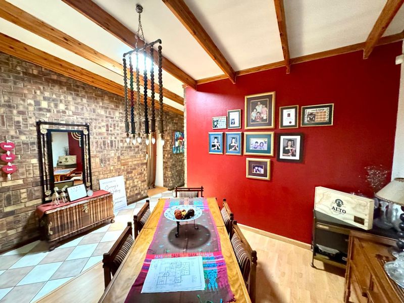 Dining room featuring exposed timber ceiling beams, a face brick feature wall, and a mix of laminate and tiled flooring.