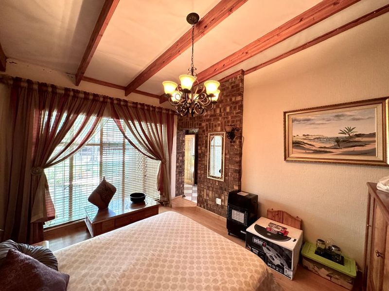A bedroom featuring exposed timber ceiling beams, a brick feature wall, and a central chandelier, offering a rustic aesthetic.