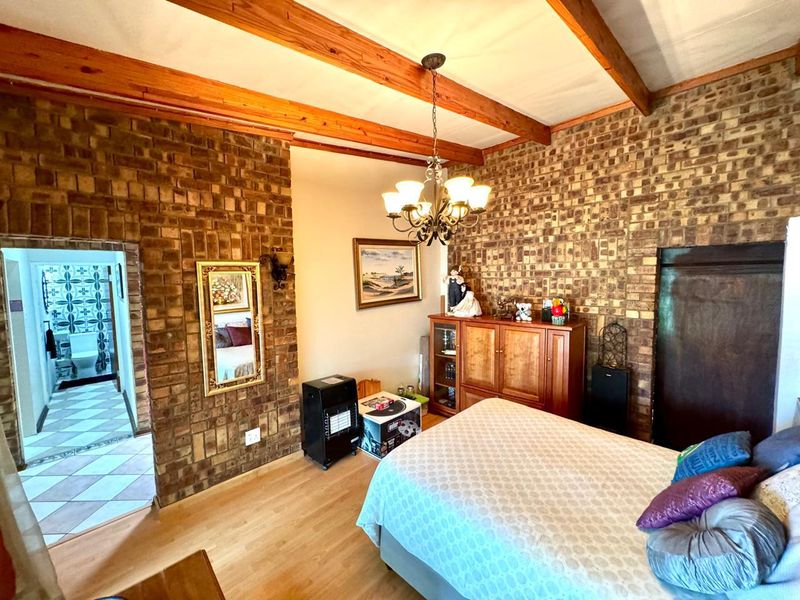 A bedroom featuring exposed brick walls and timber ceiling beams, with direct access to an adjoining bathroom.