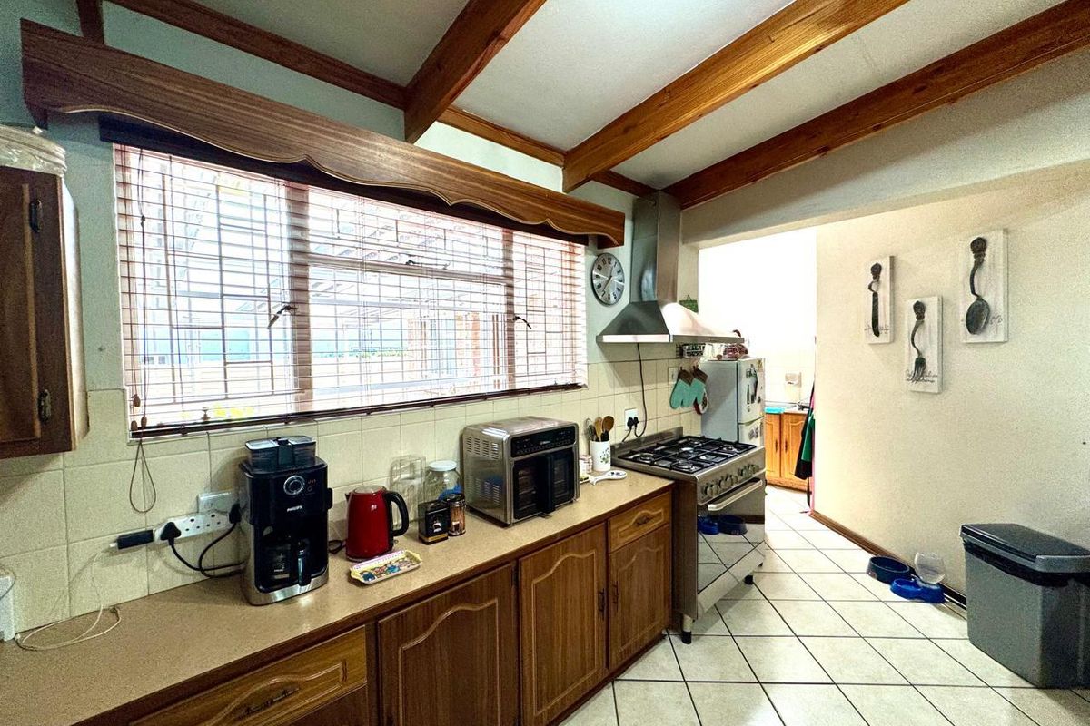 A functional kitchen featuring wooden cabinetry, gas stove with extractor fan, tiled flooring, and exposed timber ceiling beams, offering a traditional aesthetic.