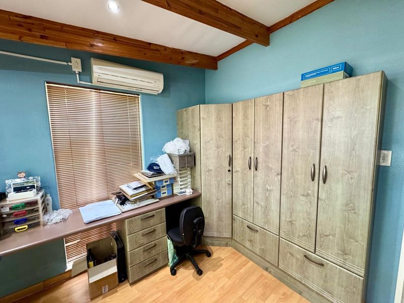 Bedroom featuring built-in wooden cabinetry, a fitted desk, laminate flooring, and exposed timber ceiling beams with an integrated air conditioning unit.