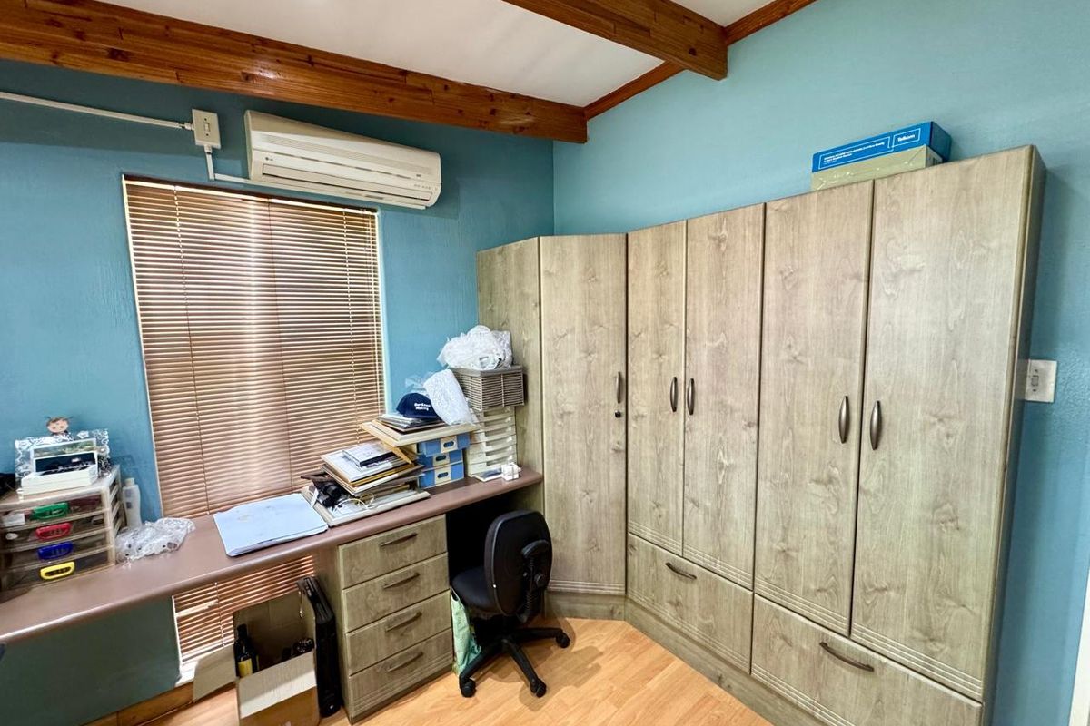 Bedroom featuring built-in wooden cabinetry, a fitted desk, laminate flooring, and exposed timber ceiling beams with an integrated air conditioning unit.
