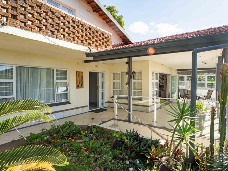 A spacious rear patio area featuring tiled flooring, a covered veranda, and a glass balustrade, overlooking a landscaped garden.