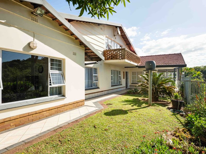 Rear view of the property featuring a tiled patio, a brick balcony, and a well-maintained garden area with established landscaping.