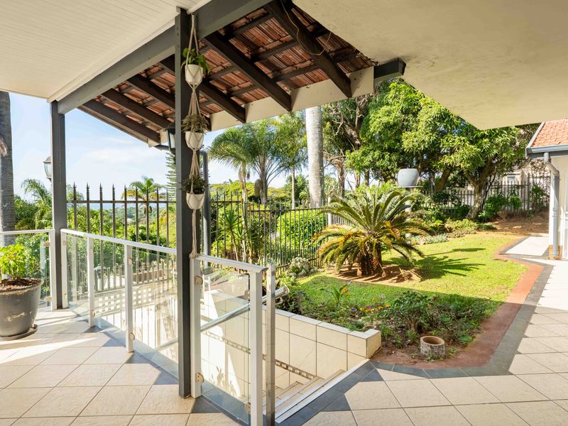 A spacious covered patio featuring tiled flooring, a glass balustrade, and direct access to a landscaped garden area.