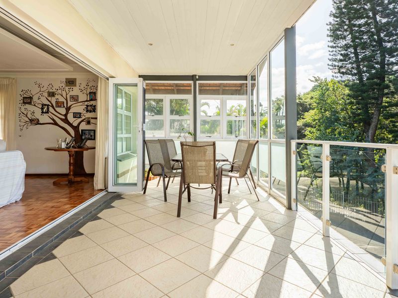 A bright, covered patio featuring tiled flooring, a modern glass balustrade, and seamless access to the interior living space through large sliding doors.