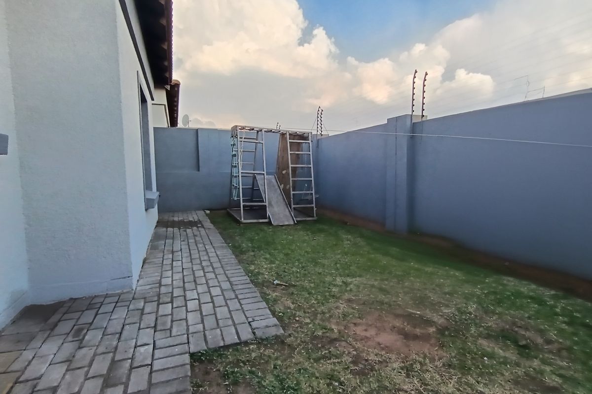 A private rear garden featuring a paved walkway, perimeter boundary walls with electric fencing, and a small grassed area.