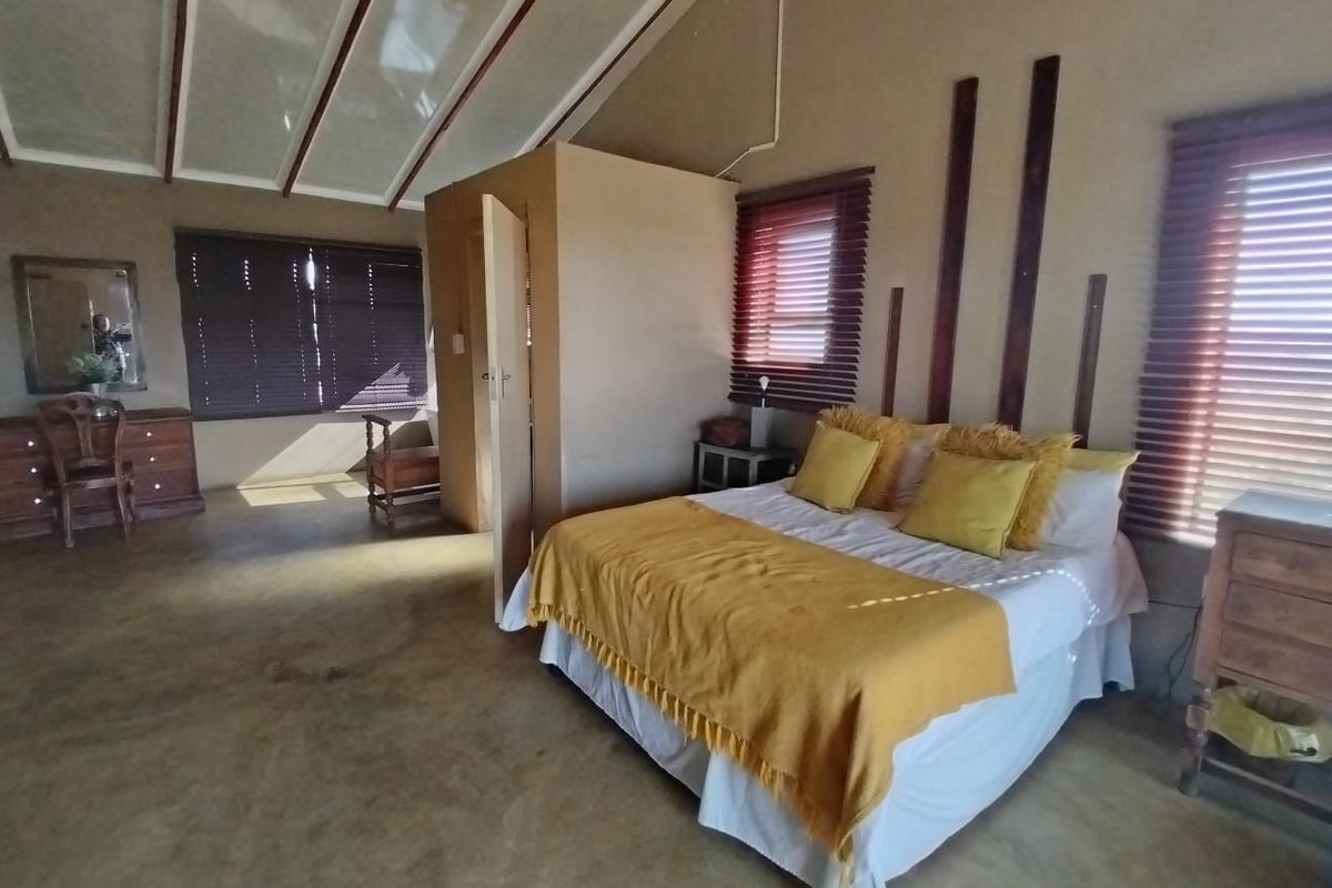 Spacious bedroom featuring exposed beam ceilings, neutral wall finishes, and large windows with fitted venetian blinds.