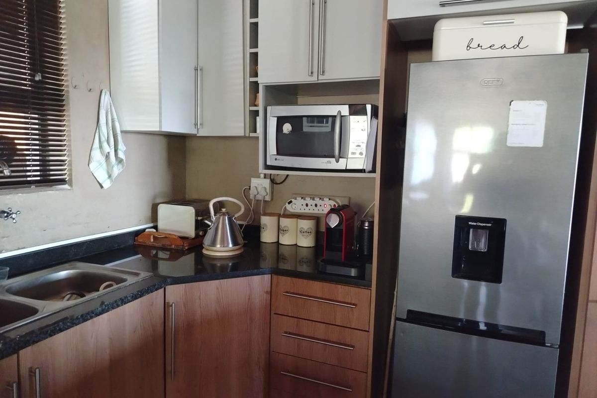 A compact kitchen featuring wood-finish lower cabinetry, white upper cabinets, granite countertops, and a built-in microwave space.