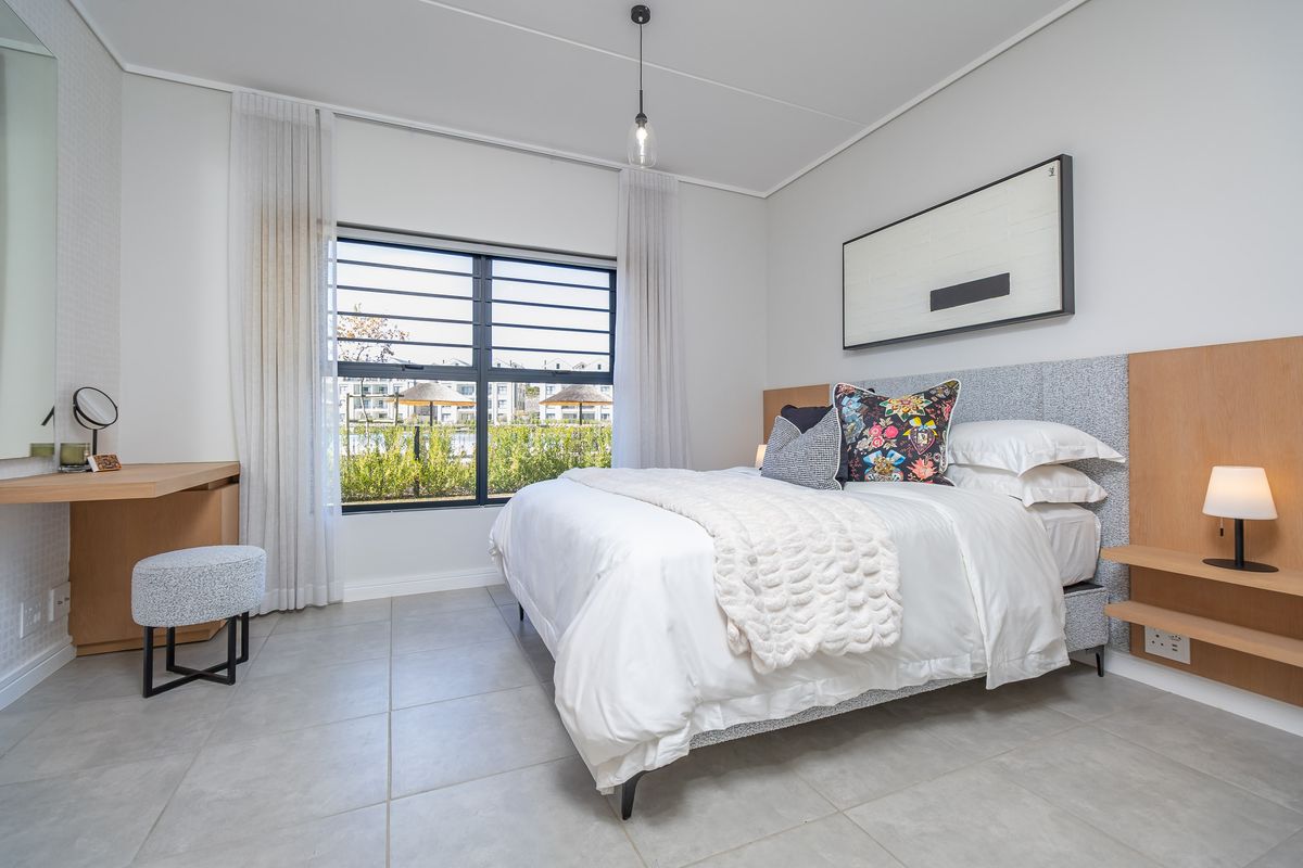 A modern, well-lit bedroom featuring tiled flooring, a built-in wooden vanity, and integrated bedside shelving with power outlets.