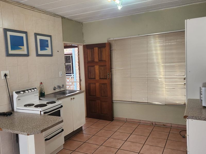 A functional kitchen featuring tiled flooring, a freestanding stove, stainless steel sink, and direct access to an outdoor area.