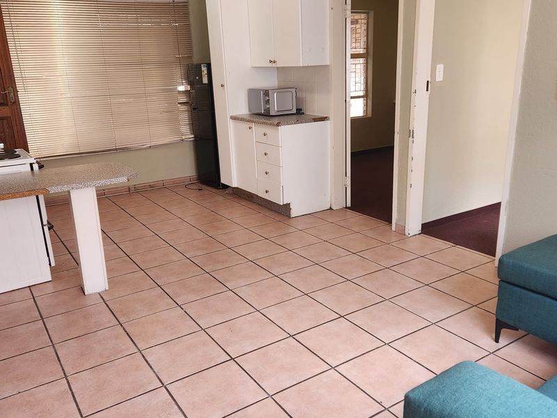 Open plan living and kitchen area featuring tiled flooring, built-in cabinetry, and natural light through venetian blinds.