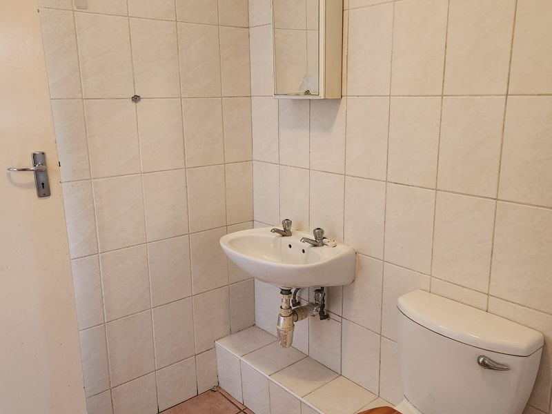 A compact bathroom featuring a wall-mounted basin, toilet, and medicine cabinet with tiled surfaces throughout.
