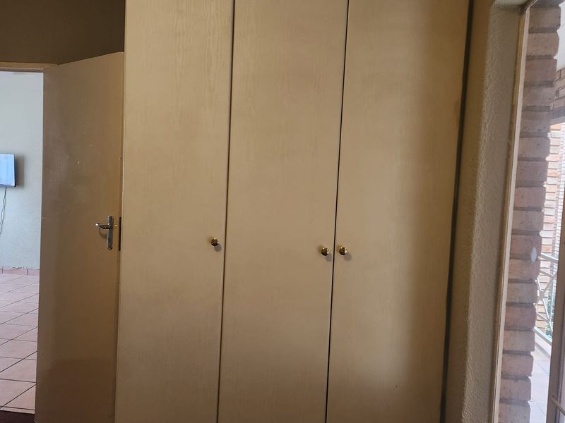 A bedroom interior featuring built-in cupboards and a window, showing signs of age and wear on the cabinetry and finishes.