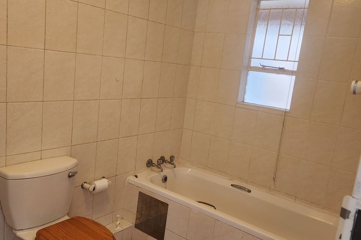 A functional bathroom featuring a standard bathtub, toilet, and full-height wall tiling, requiring cosmetic updates to modernize the space.