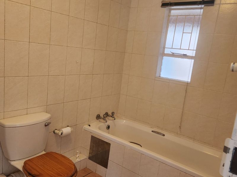 A functional bathroom featuring a standard bathtub, toilet, and full-height wall tiling, requiring cosmetic updates to modernize the space.