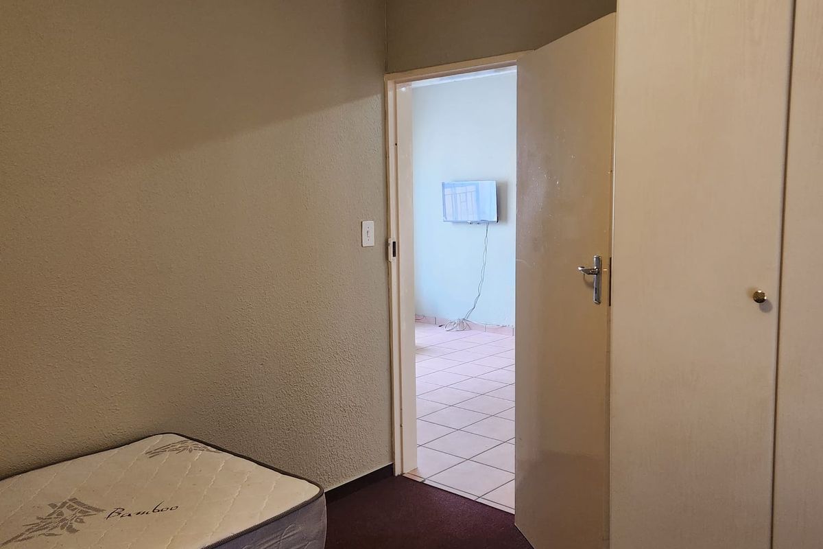 A bedroom featuring built-in wardrobes and carpeted flooring, with an open doorway leading to an adjacent tiled room.