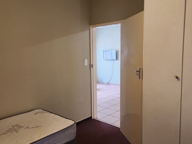 A bedroom featuring built-in wardrobes and carpeted flooring, with an open doorway leading to an adjacent tiled room.