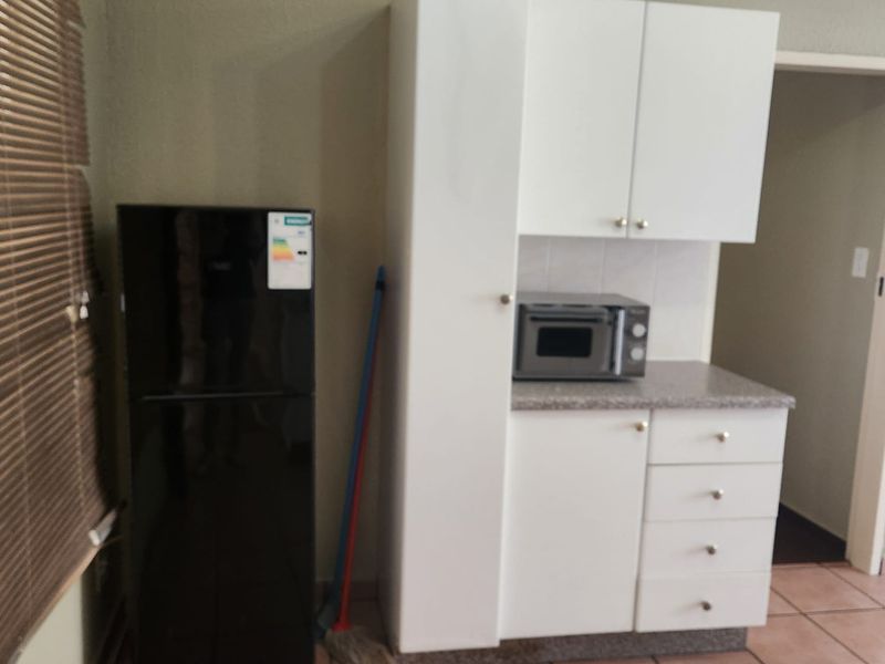 A compact kitchen area featuring white built-in cabinetry, laminate countertops, and tiled flooring, providing functional storage and preparation space.