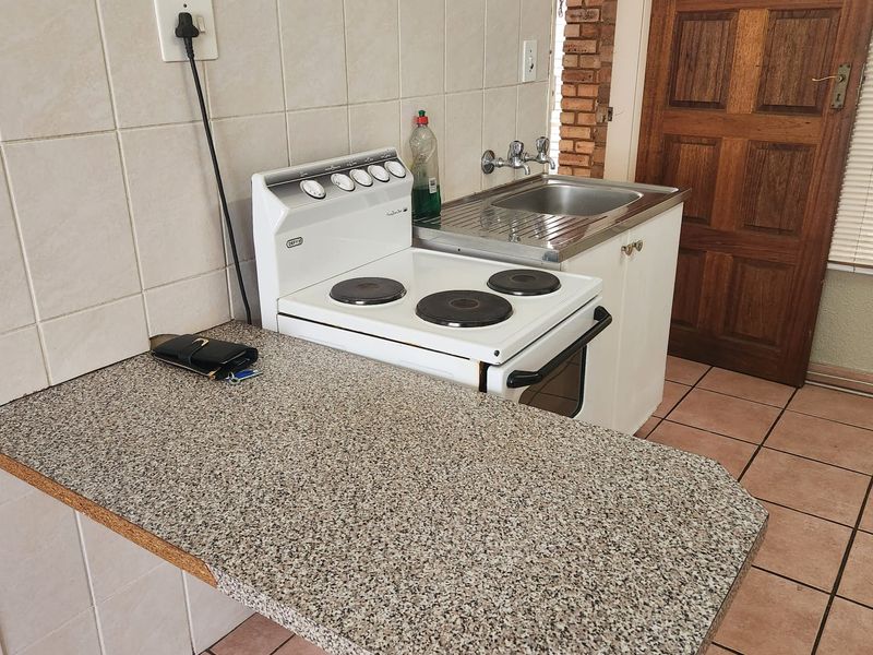 A compact kitchen area featuring a freestanding stove, stainless steel sink, tiled backsplash, and laminate countertop with ceramic floor tiles.