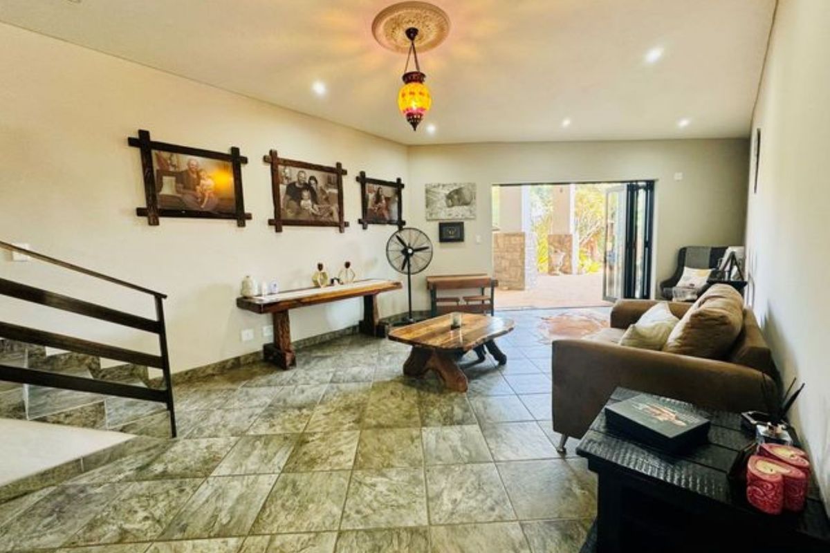 Spacious living area featuring tiled flooring, a decorative ceiling rose with pendant lighting, and bi-fold doors opening to an outdoor patio space.