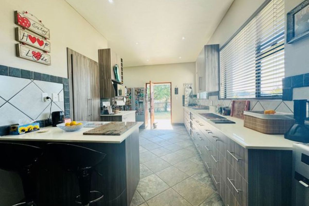 Modern kitchen featuring wood-grain cabinetry, stone countertops, tiled flooring, and recessed lighting, with direct access to the rear exterior.