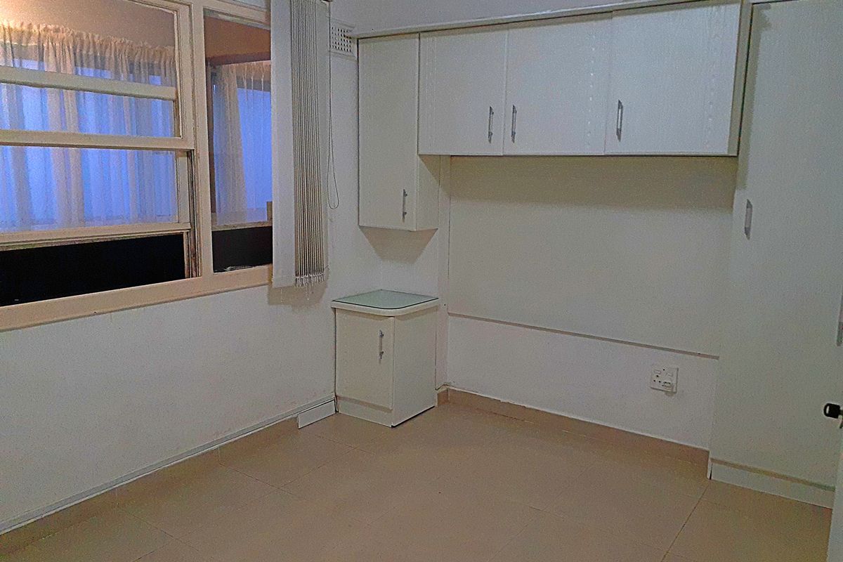 An empty bedroom featuring tiled flooring, built-in cabinetry, and a sliding window with vertical blinds, offering a blank canvas for potential updates.