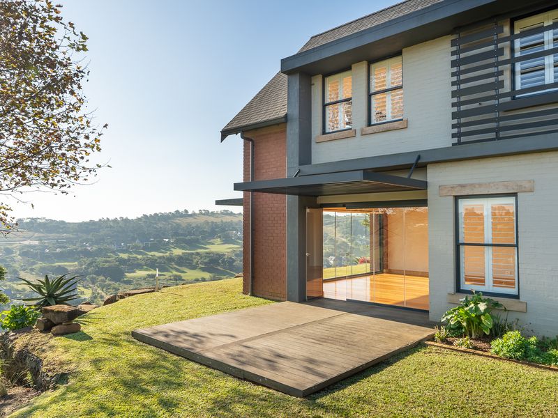 Rear view of the property featuring a timber deck, modern sliding glass doors, and a well-maintained brick and painted facade overlooking the landscape.