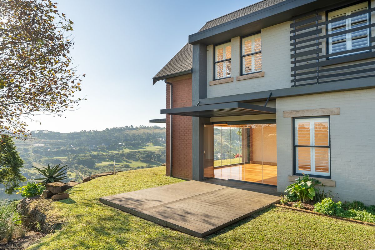 Rear view of the property featuring a timber deck, modern sliding glass doors, and a well-maintained brick and painted facade overlooking the landscape.