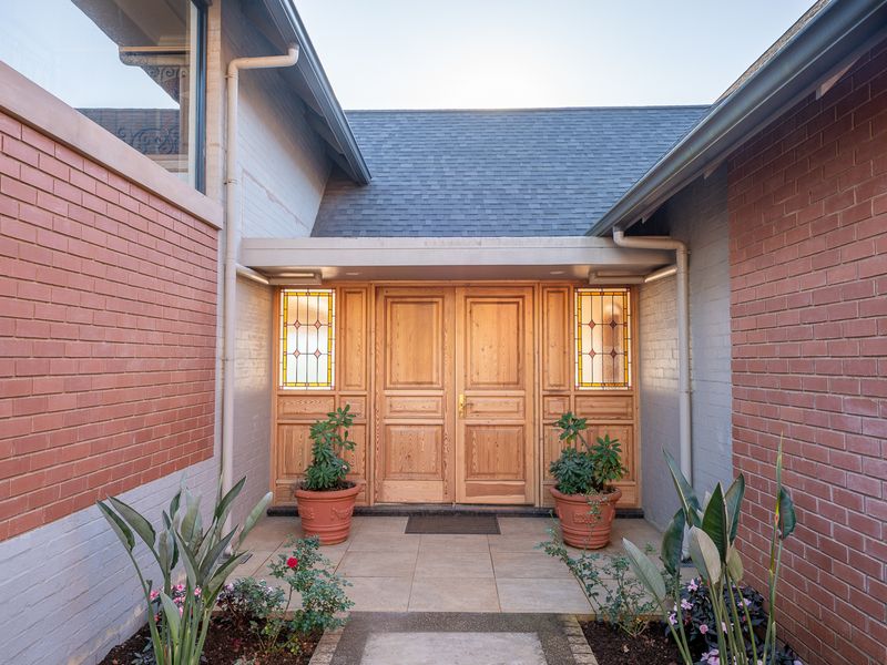 A welcoming front entrance featuring double timber doors with stained glass sidelights, set within a well-maintained brick facade and tiled porch area.