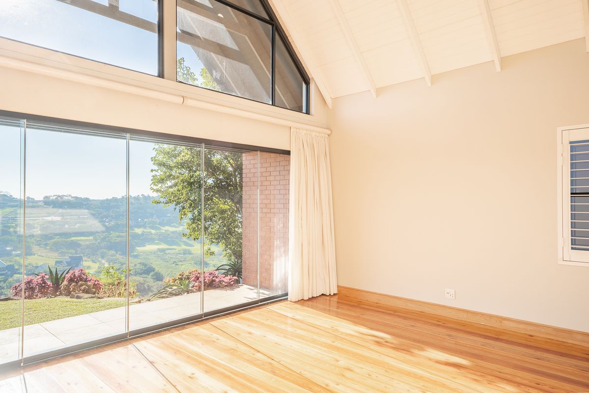 Bright and airy living space featuring vaulted ceilings with exposed rafters, polished timber flooring, and expansive frameless glass doors offering scenic views.