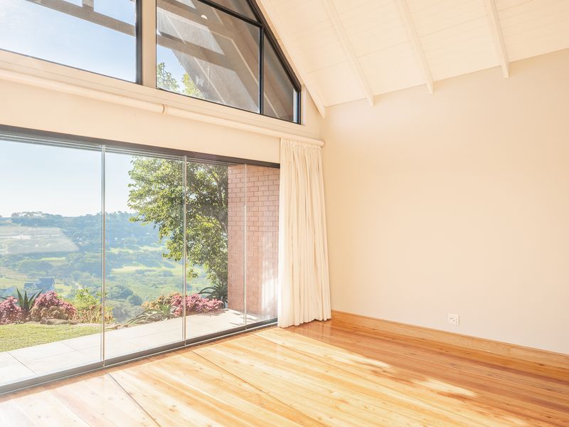 Bright and airy living space featuring vaulted ceilings with exposed rafters, polished timber flooring, and expansive frameless glass doors offering scenic views.