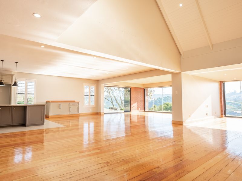 Spacious open-plan living area featuring vaulted ceilings, polished hardwood floors, a modern kitchen island, and expansive sliding glass doors with scenic views.