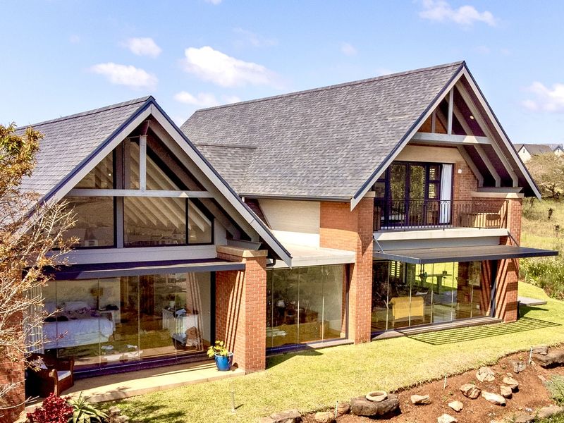 A modern architectural rear elevation featuring exposed timber trusses, extensive floor-to-ceiling glass walls, brick masonry, and a spacious upper-level balcony.