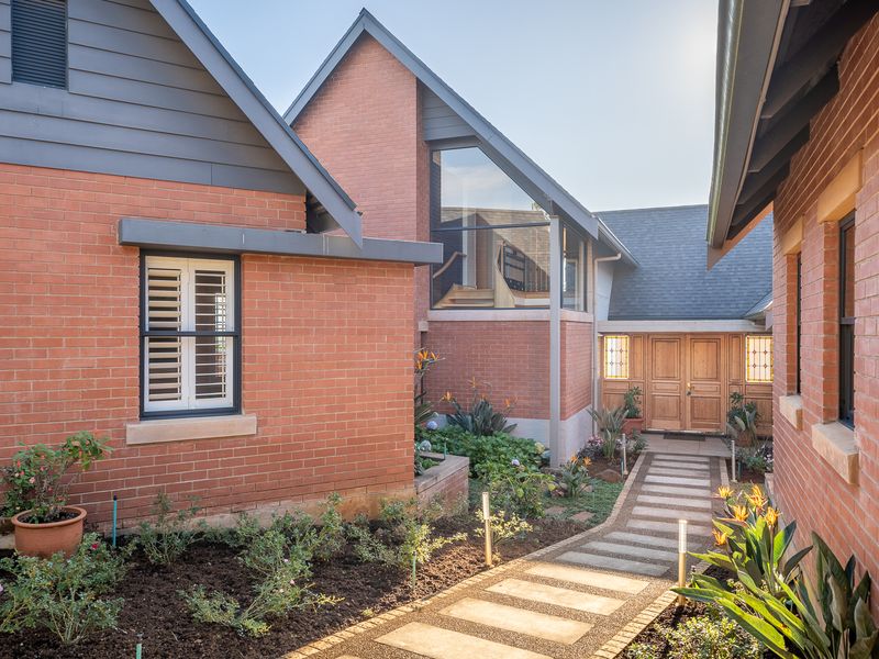 A well-maintained front entrance featuring a brick facade, timber double doors, and a stone pathway leading through a landscaped garden.