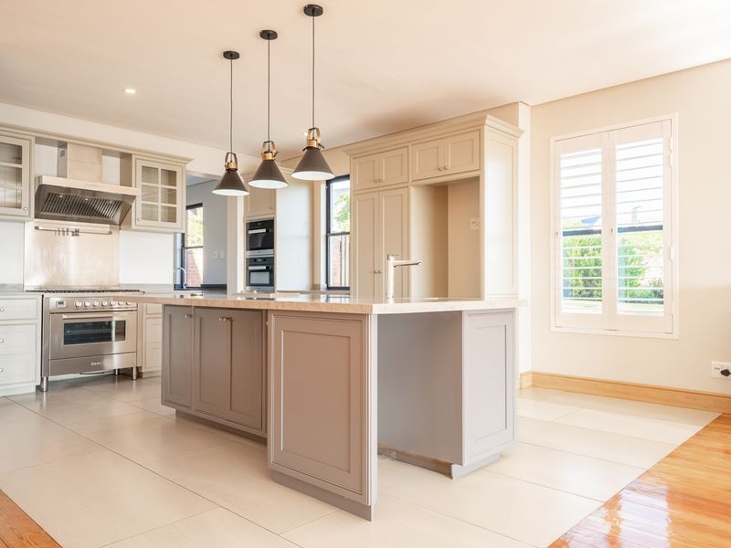 A modern, spacious kitchen featuring a central island, shaker-style cabinetry, high-end built-in appliances, and elegant pendant lighting, finished with neutral tones and tiled flooring.