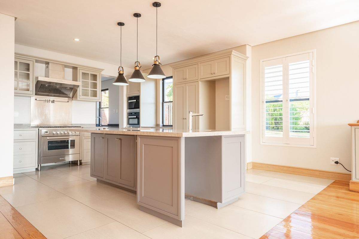 A modern, spacious kitchen featuring a central island, shaker-style cabinetry, high-end built-in appliances, and elegant pendant lighting, finished with neutral tones and tiled flooring.