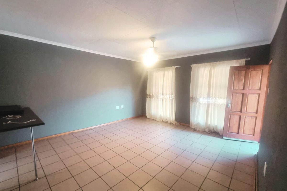 A spacious living room featuring tiled flooring, a ceiling light fixture, and direct access to the exterior through a wooden door.