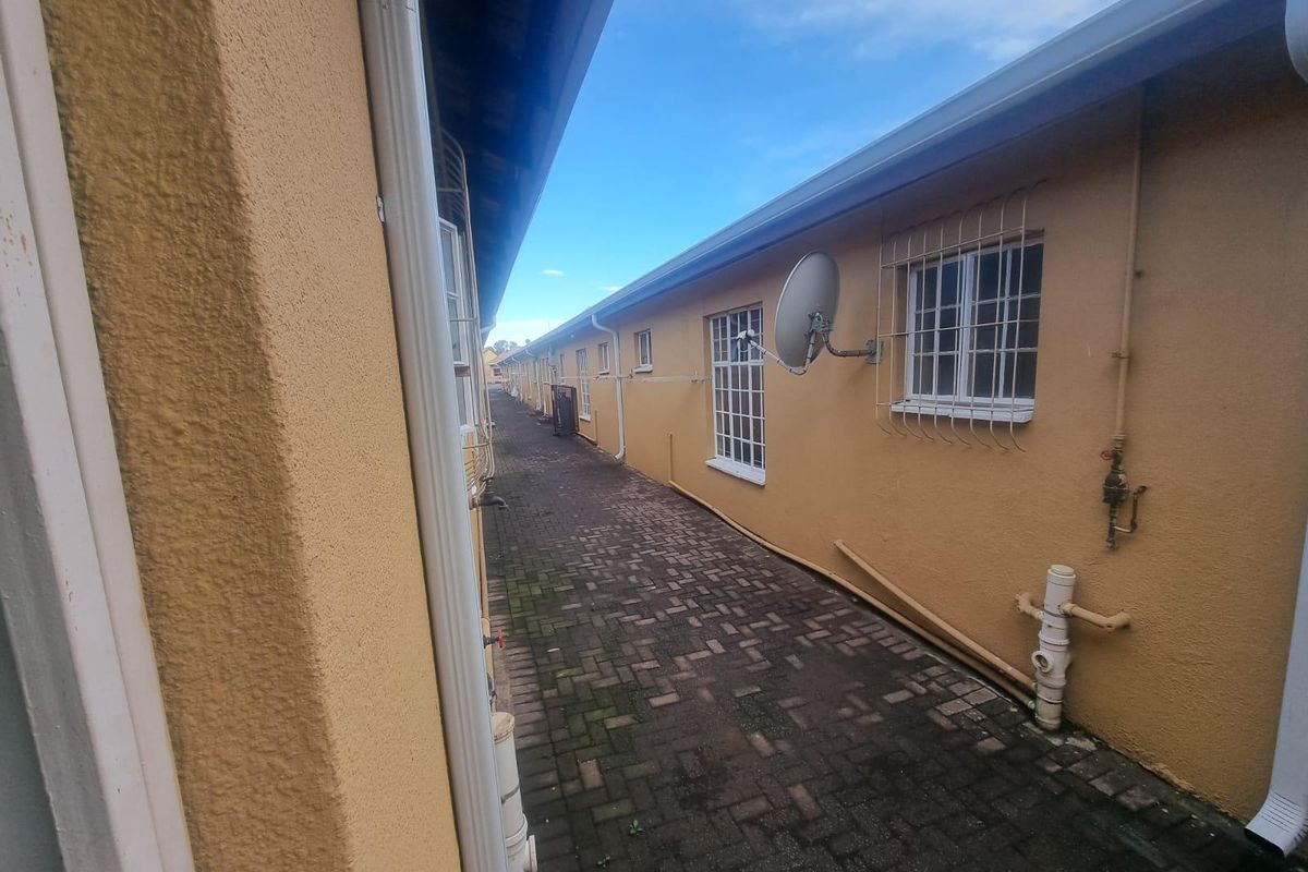 A narrow exterior side passage featuring paved flooring, security bars on windows, and external plumbing fixtures along the townhouse wall.