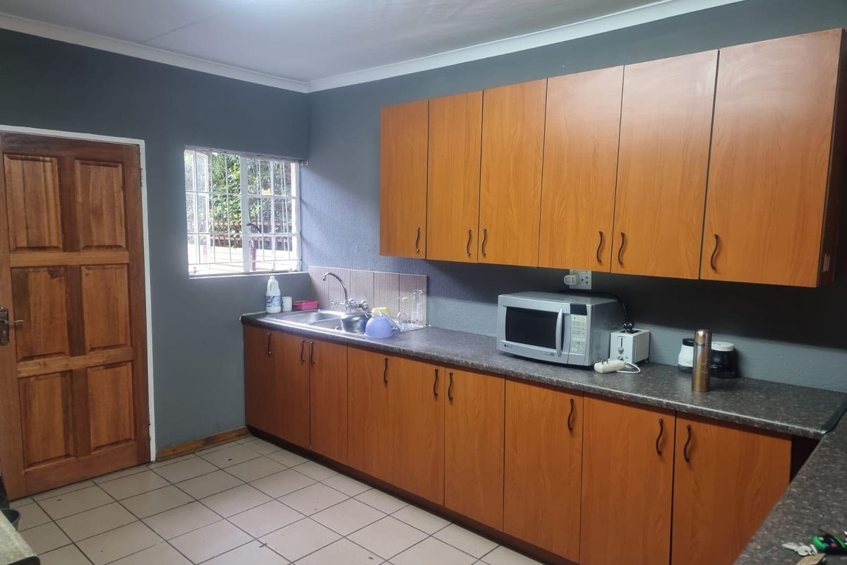 A functional kitchen featuring wood-finish cabinetry, laminate countertops, a stainless steel sink, and tiled flooring with a window for natural light.
