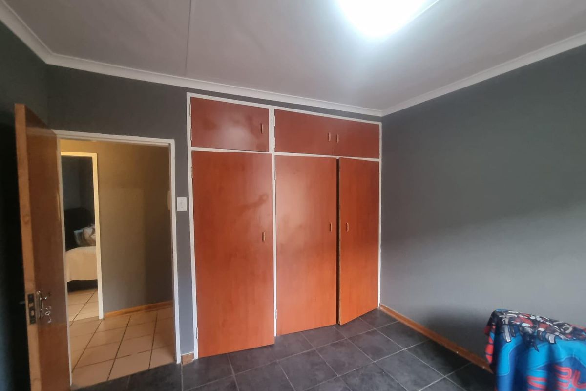 A bedroom featuring built-in wooden cupboards, dark floor tiling, and a doorway leading to an adjacent room.