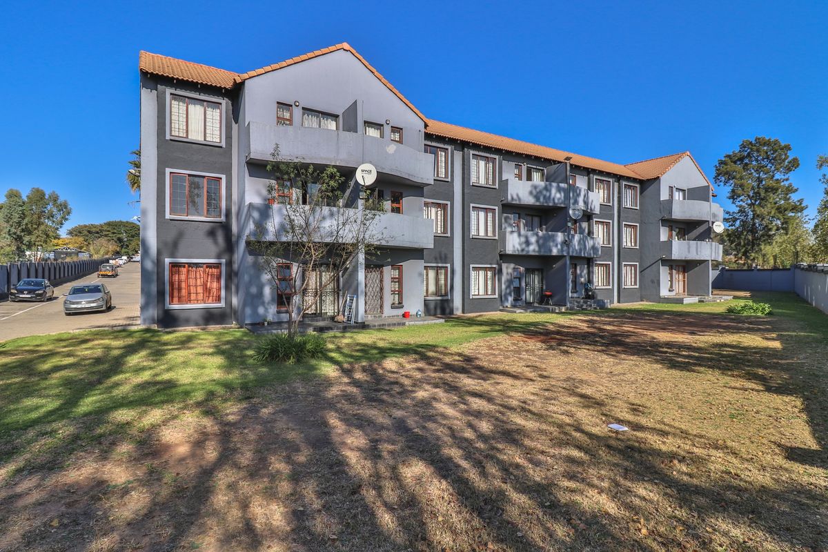Rear view of a multi-story apartment complex featuring private balconies, tiled roofing, and a shared garden area.