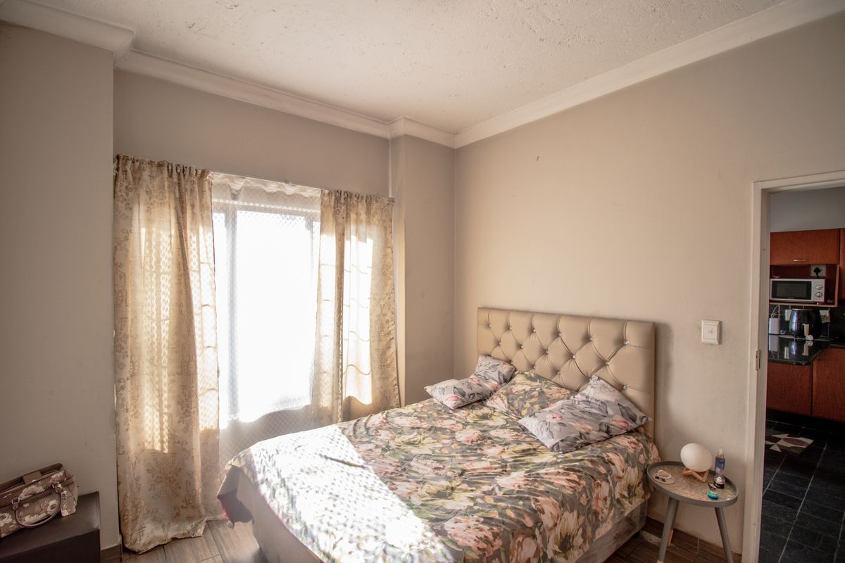 A bedroom featuring tiled flooring and coving, with visible signs of wear on the ceiling and walls.
