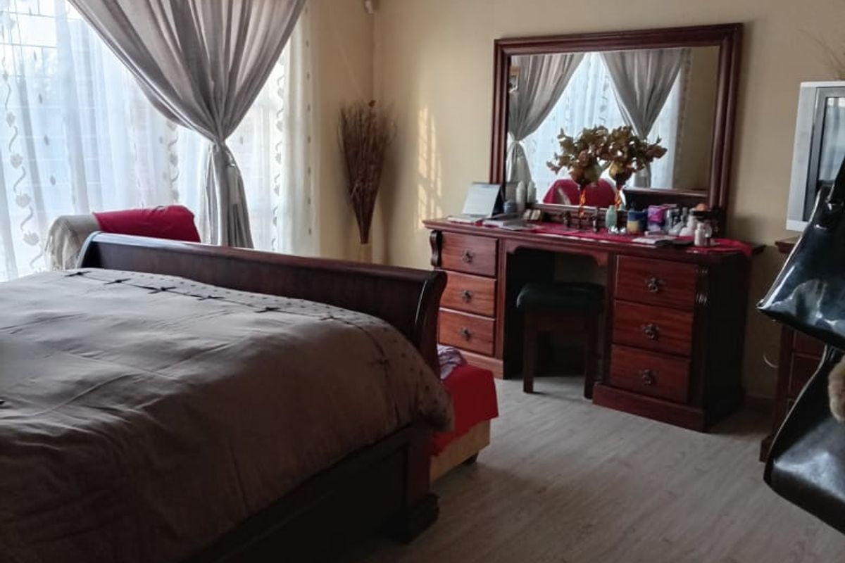 A well-lit bedroom featuring light-toned laminate flooring, decorative ceiling cornices, and large windows with curtain tracks.