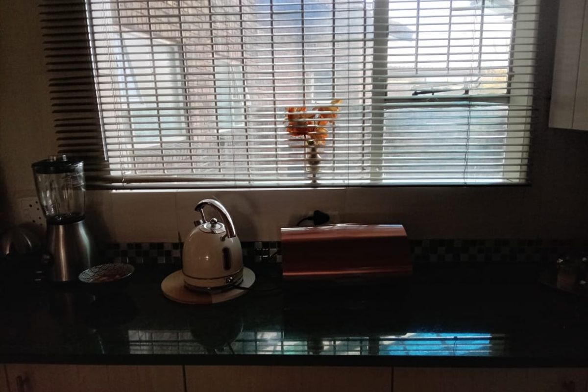 A kitchen counter area featuring dark stone countertops, tiled backsplash, and horizontal window blinds.
