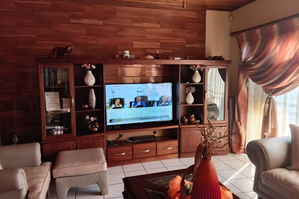 A living room featuring a wood-paneled accent wall, built-in wooden cabinetry, and tiled flooring with natural light from the adjacent window.