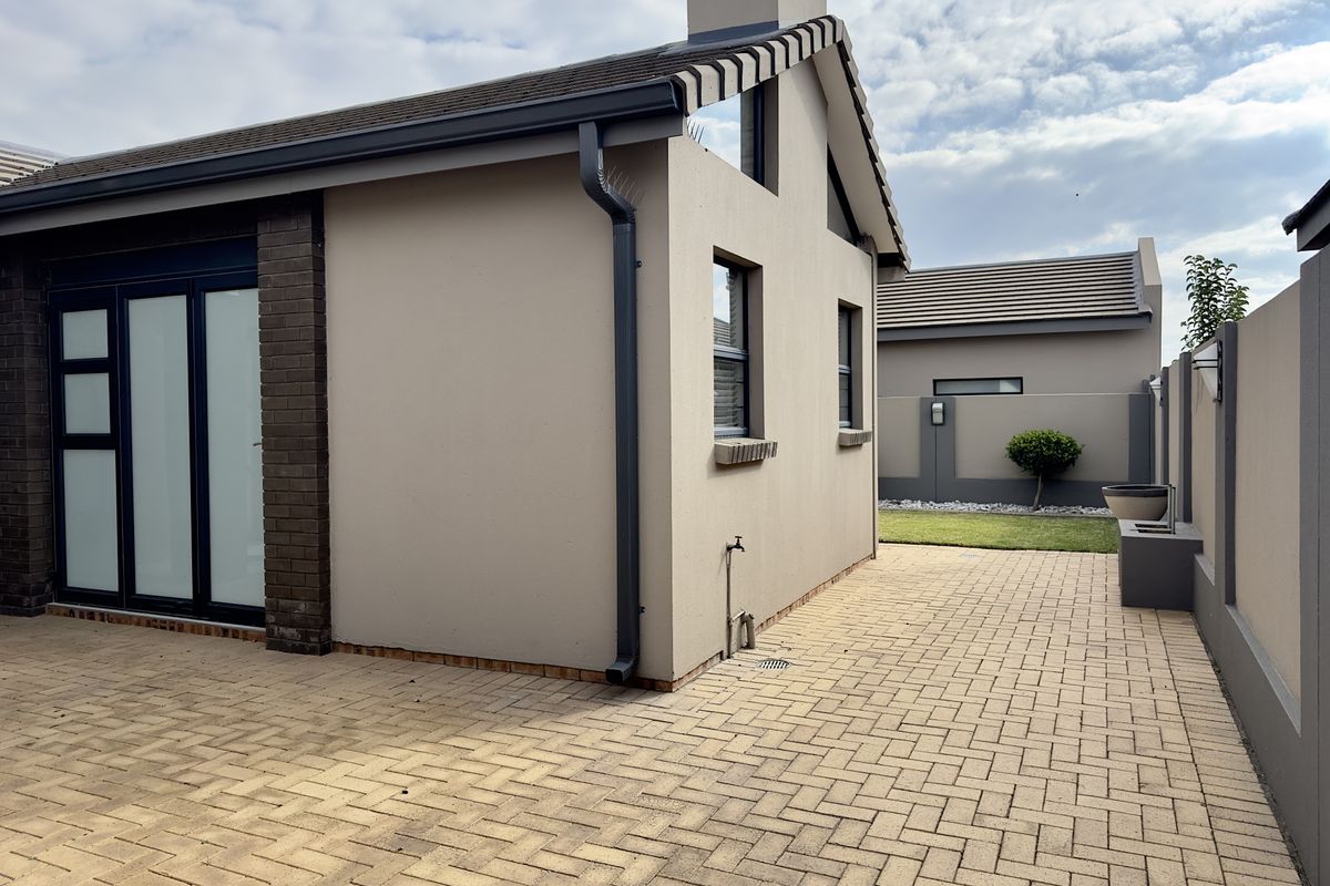 Rear view of the property featuring a paved patio area, modern exterior finishes, and a well-maintained boundary wall.