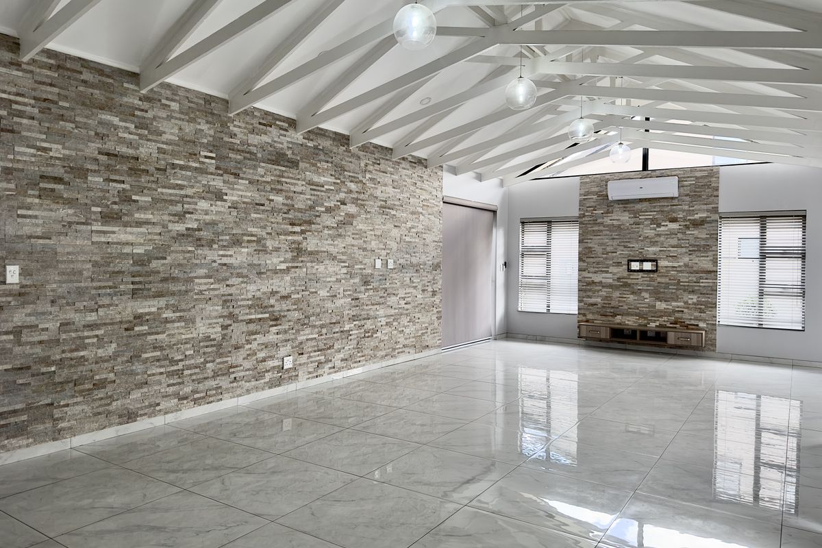 Spacious living area featuring high vaulted ceilings with exposed beams, polished porcelain floor tiles, and a striking natural stone feature wall.