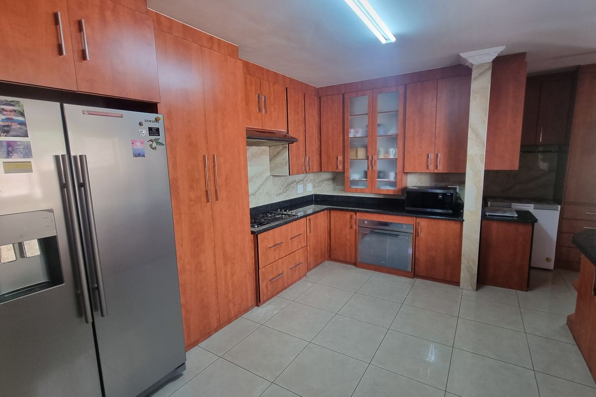 A spacious kitchen featuring warm-toned wooden cabinetry, granite countertops, a gas hob, built-in oven, and tiled flooring with ample storage space.